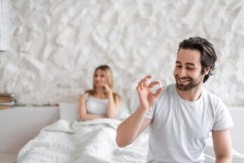 young man holding pill solving sexual dysfunction problems happy woman sitting bed waiting