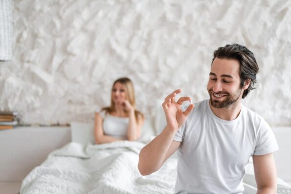 young man holding pill solving sexual dysfunction problems happy woman sitting bed waiting